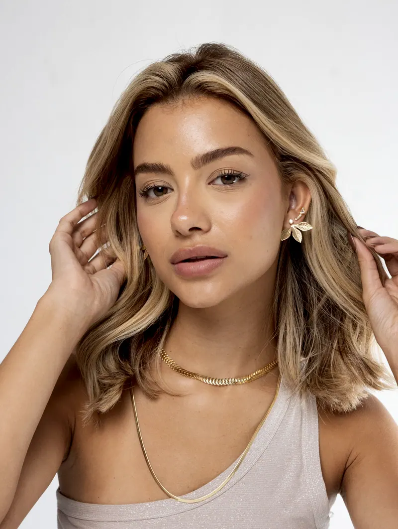 Modelo com brinco de folhas dourado e colar dourado trançado