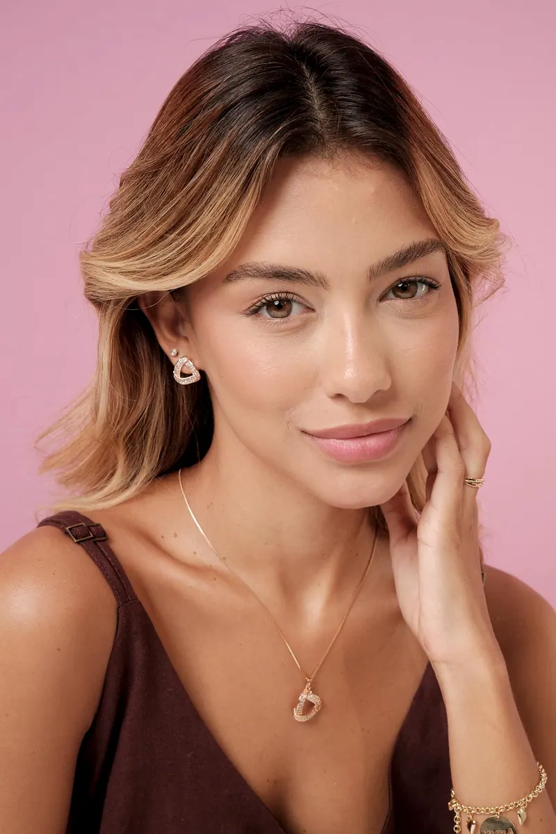 Modelo sorrindo com brinco e colar de zircônias em formato de triângulo